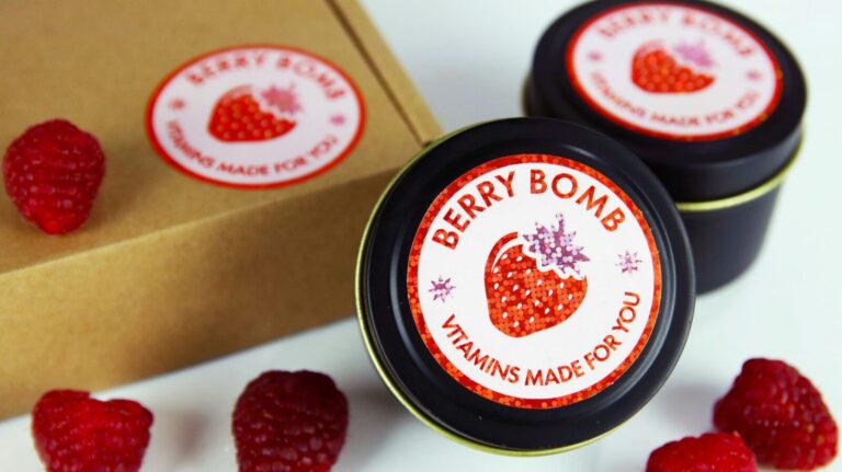 Round custom product labels on black supplement tins with fresh raspberries